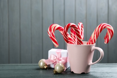 Photo of Many sweet candy canes in cup, gift box and Christmas decor on grey wooden table. Space for text