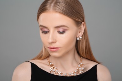 Beautiful young woman with elegant jewelry on gray background