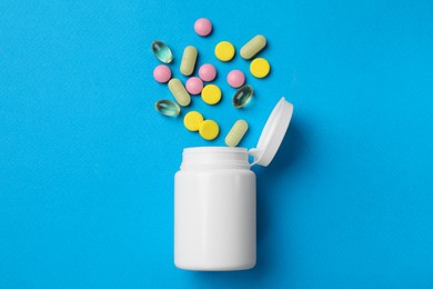 Photo of Different vitamin pills and bottle on light blue background, top view