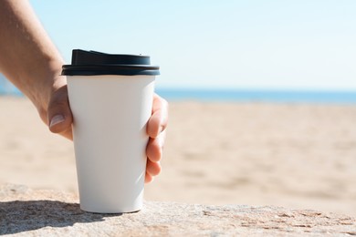 Photo of Woman with takeaway coffee cup on beach, closeup. Space for text