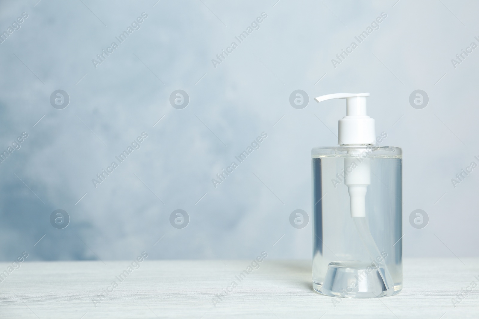 Photo of Dispenser bottle with antiseptic gel on table against light background. Space for text