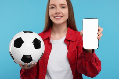 Happy sports fan with ball and smartphone on light blue background, selective focus