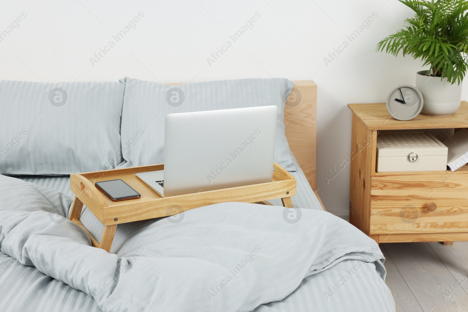 Photo of Wooden tray table with laptop and smartphone on bed indoors