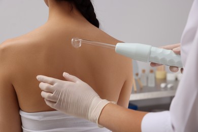 Photo of Woman undergoing physiotherapy procedure with darsonval in salon, back view