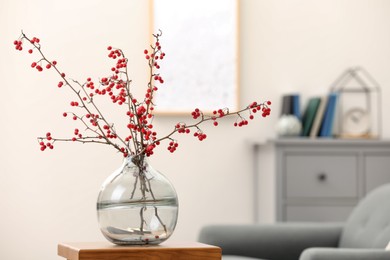 Photo of Hawthorn branches with red berries on wooden table in living room