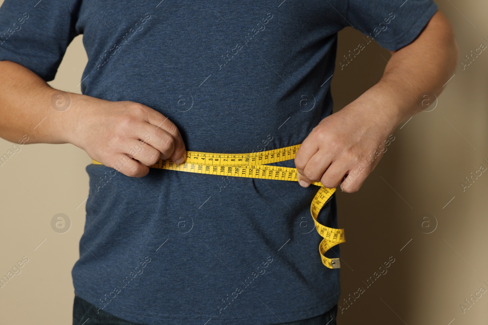Photo of Man measuring waist with tape on beige background, closeup