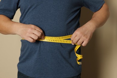 Man measuring waist with tape on beige background, closeup