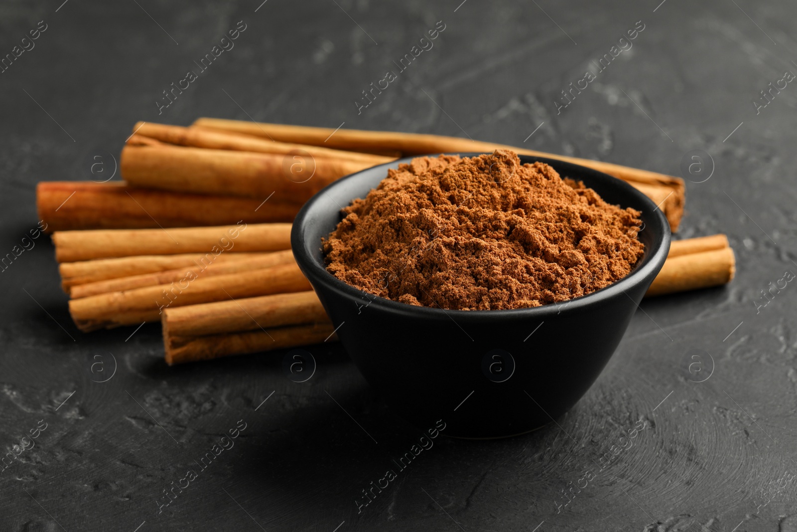 Photo of Aromatic cinnamon powder and sticks on black table, closeup