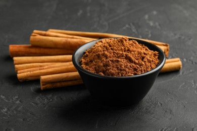 Aromatic cinnamon powder and sticks on black table, closeup