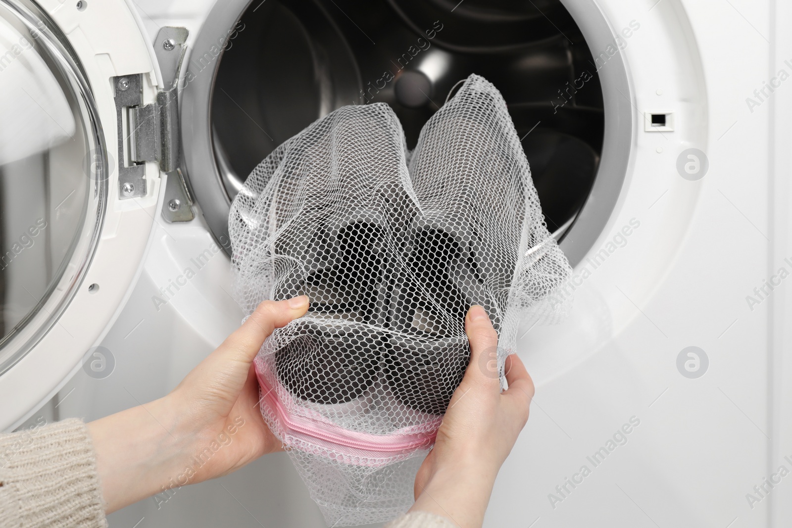 Photo of Woman putting stylish sneakers into washing machine, closeup