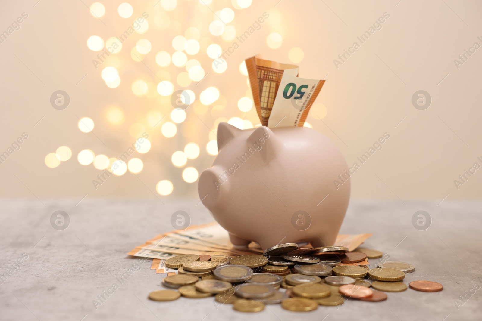 Photo of Piggy bank with euro banknote and coins on grey table against blurred lights, space for text