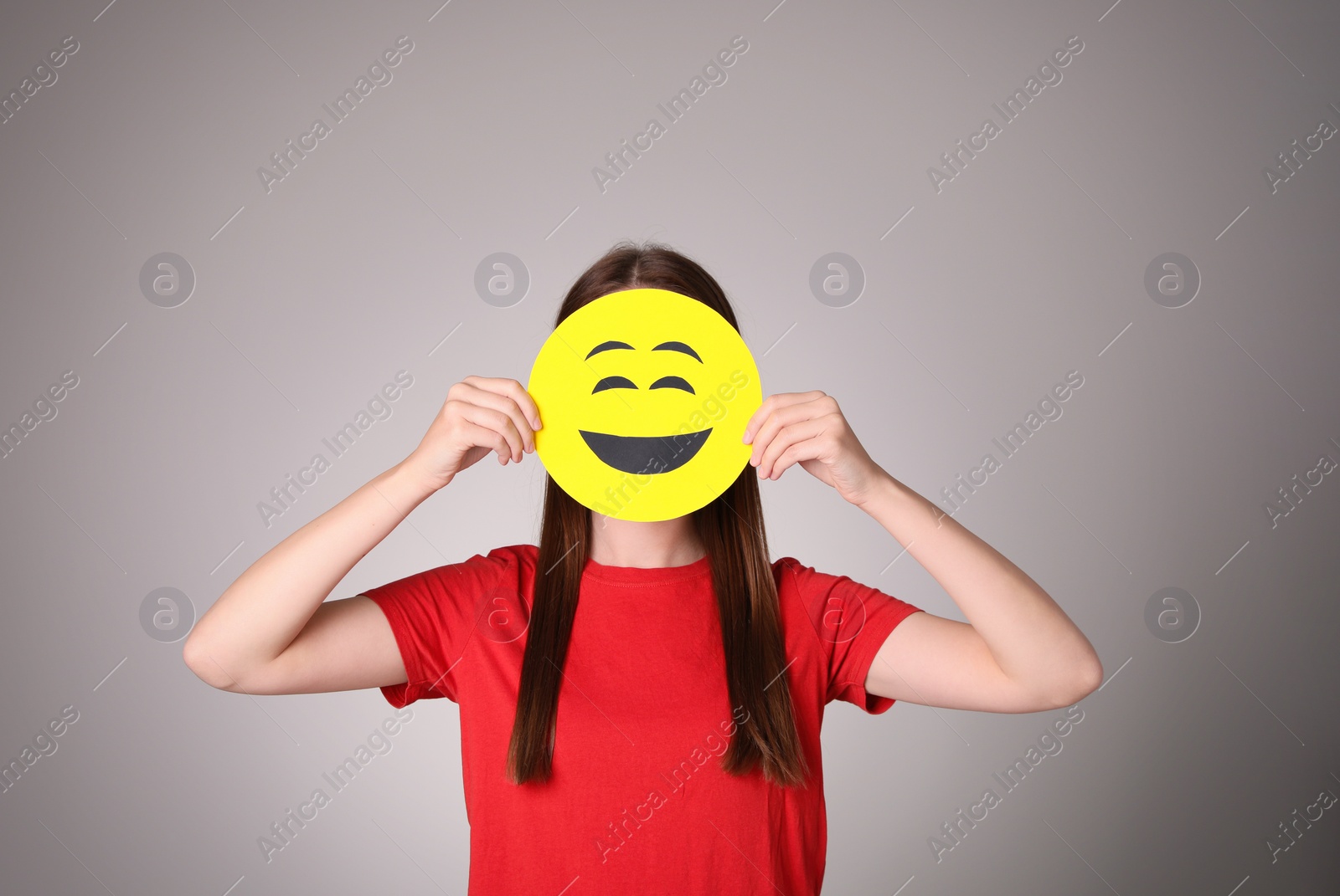 Photo of Woman covering face with laughing emoji on grey background