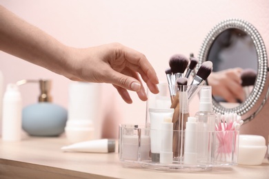 Photo of Woman taking cosmetic products from holder on dressing table, closeup
