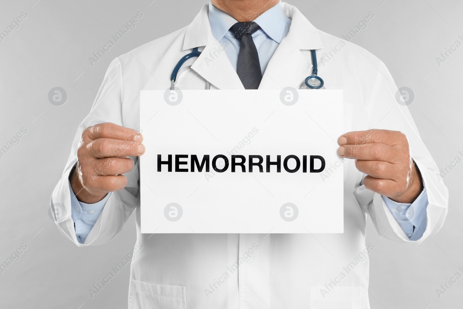 Photo of Doctor holding sign with word HEMORRHOID on light grey background, closeup