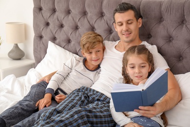 Photo of Father reading book with children in bedroom. Happy family