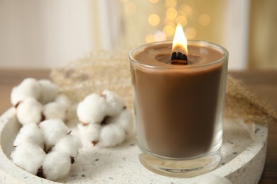 Photo of Burning candle with wooden wick in glass holder near cotton flowers on white tray