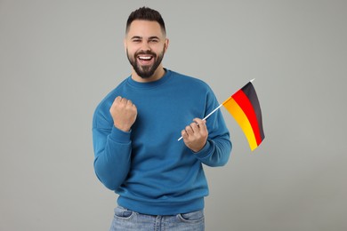 Emotional young man holding flag of Germany on light grey background