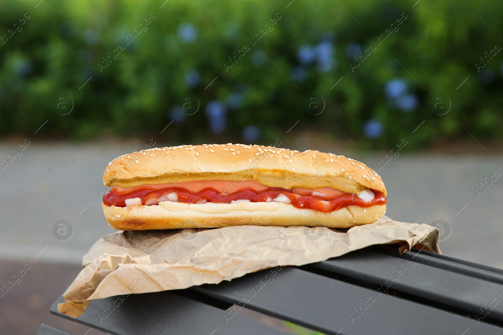 Photo of Fresh delicious hot dog with sauce on black bench outdoors