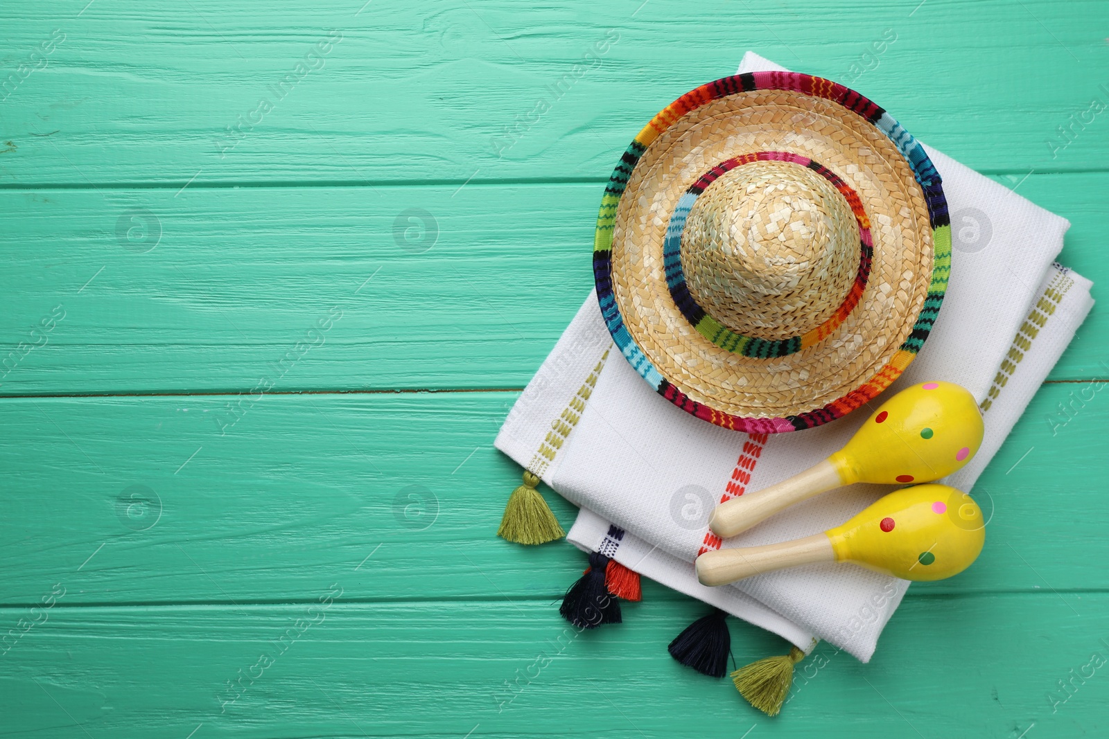 Photo of Mexican sombrero hat, maracas and poncho on turquoise wooden table, flat lay. Space for text