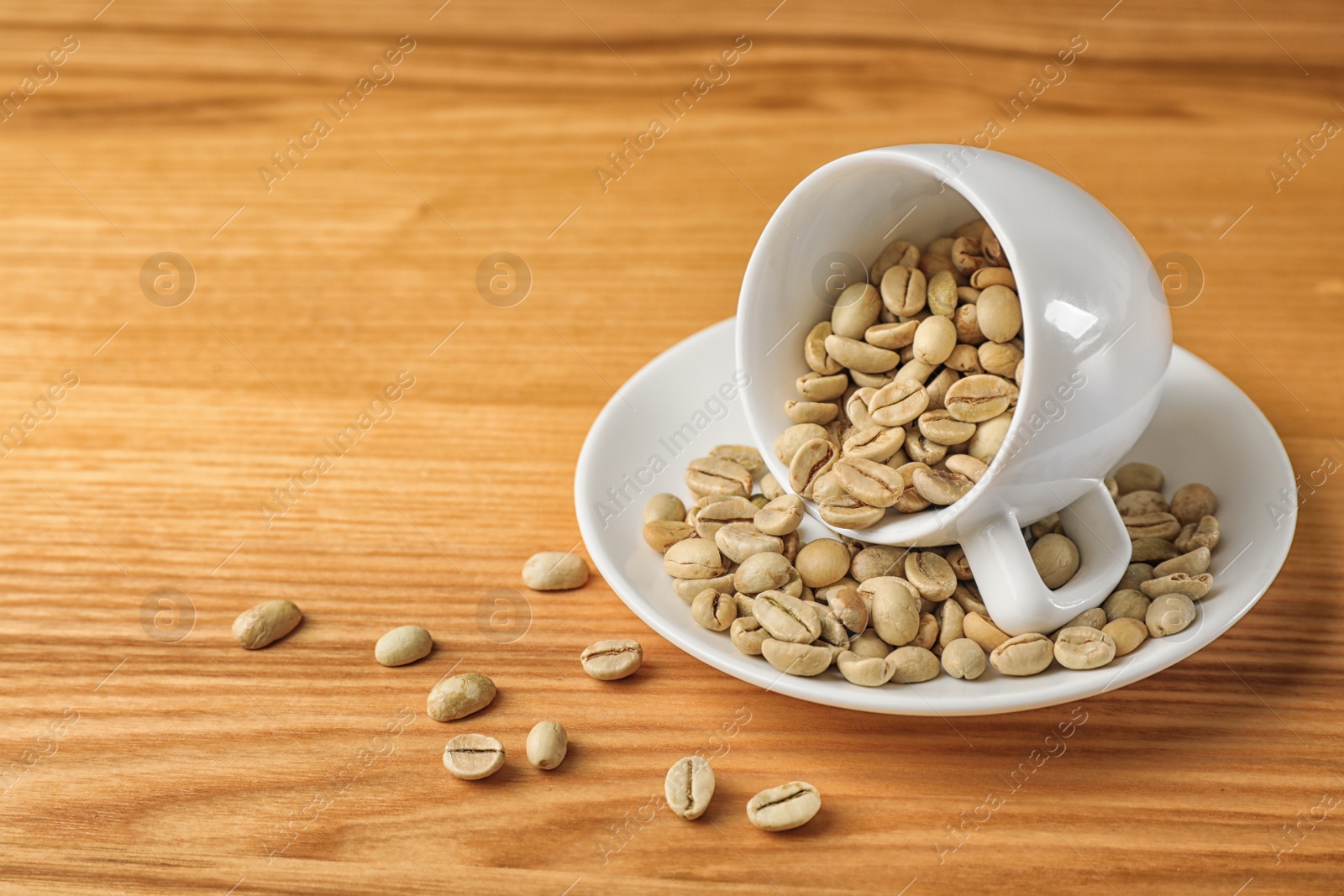 Photo of Cup and saucer with green coffee beans on wooden background. Space for text