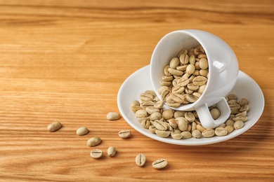 Photo of Cup and saucer with green coffee beans on wooden background. Space for text