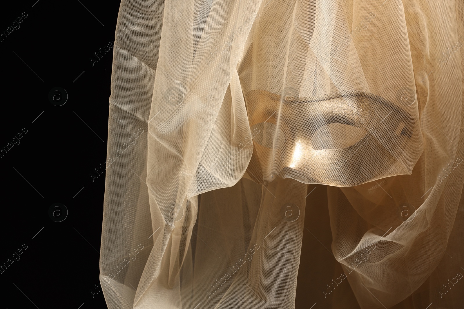 Photo of Theatrical performance. Elegant face mask and beige tulle fabric on black background