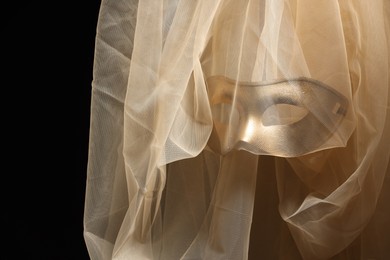 Theatrical performance. Elegant face mask and beige tulle fabric on black background