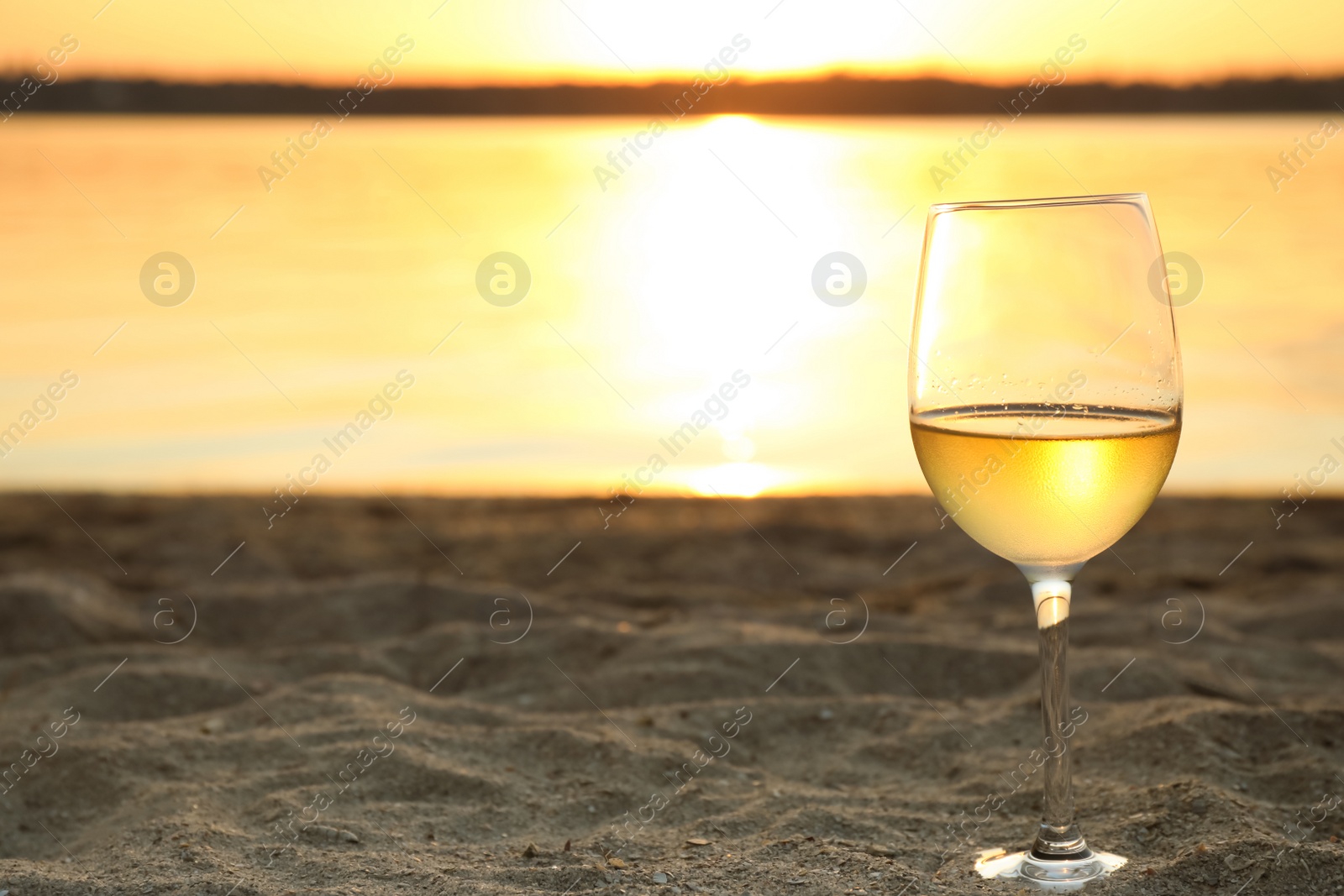 Photo of Glass of delicious wine on riverside at sunset