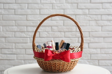 Photo of Wicker gift basket with cosmetic products on table near white brick wall