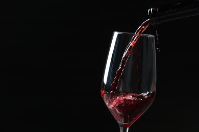 Photo of Pouring red wine into glass against black background, closeup. Space for text