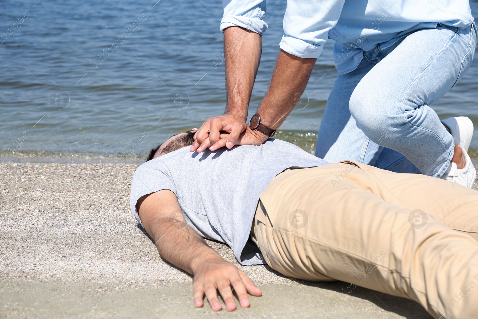 Photo of Passerby performing CPR on unconscious young man near sea. First aid