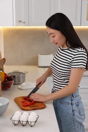 Cooking process. Beautiful woman cutting tomato in kitchen