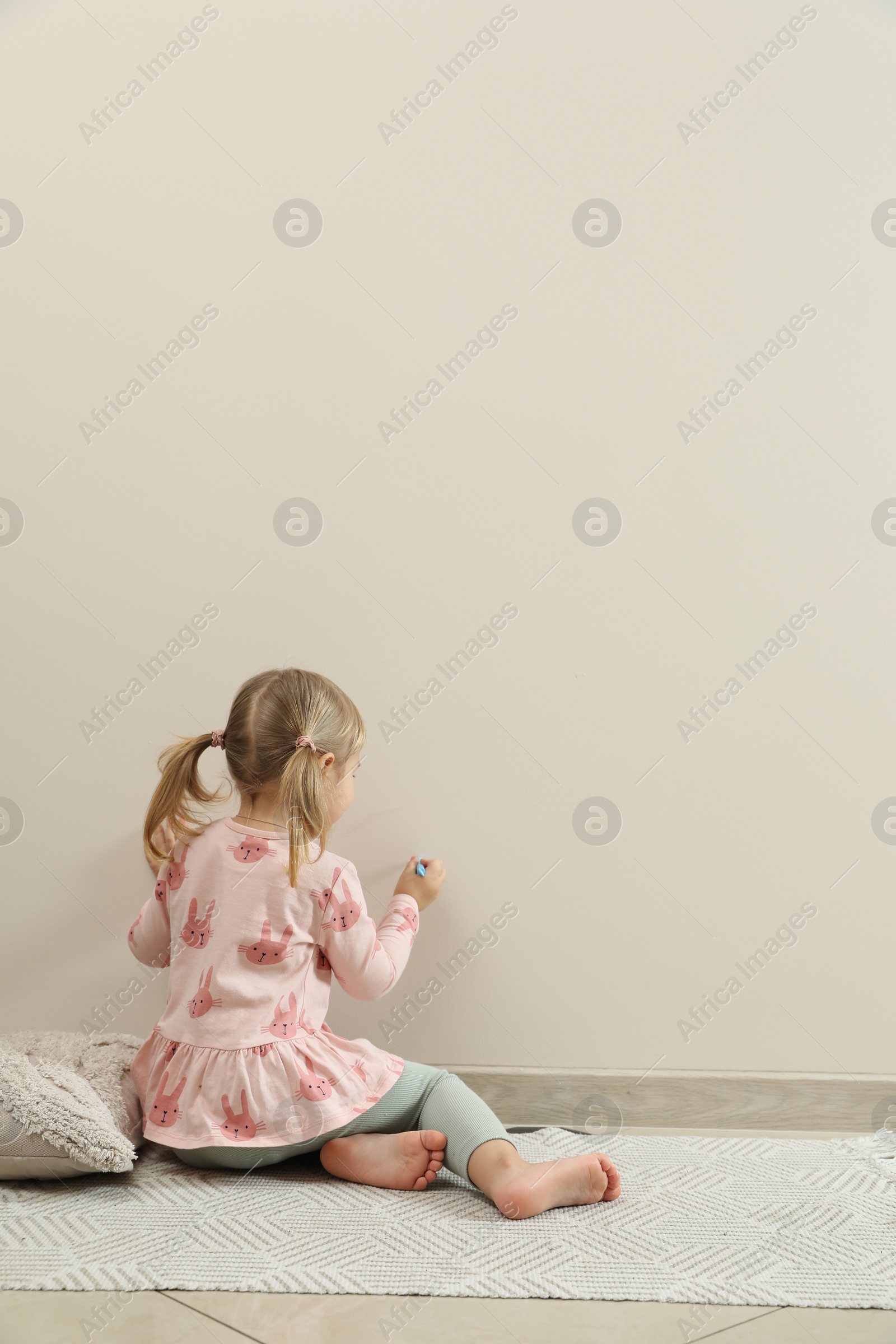 Photo of Little girl drawing on beige wall indoors, back view and space for text. Child`s art