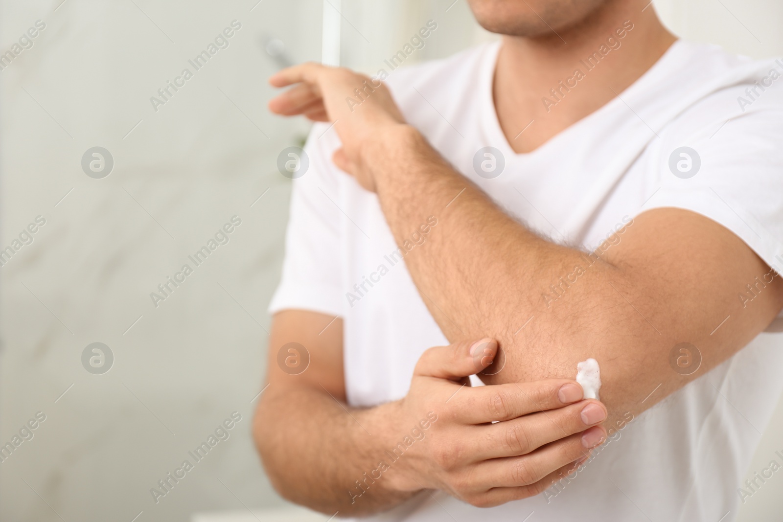 Photo of Man applying cream onto elbow indoors, closeup