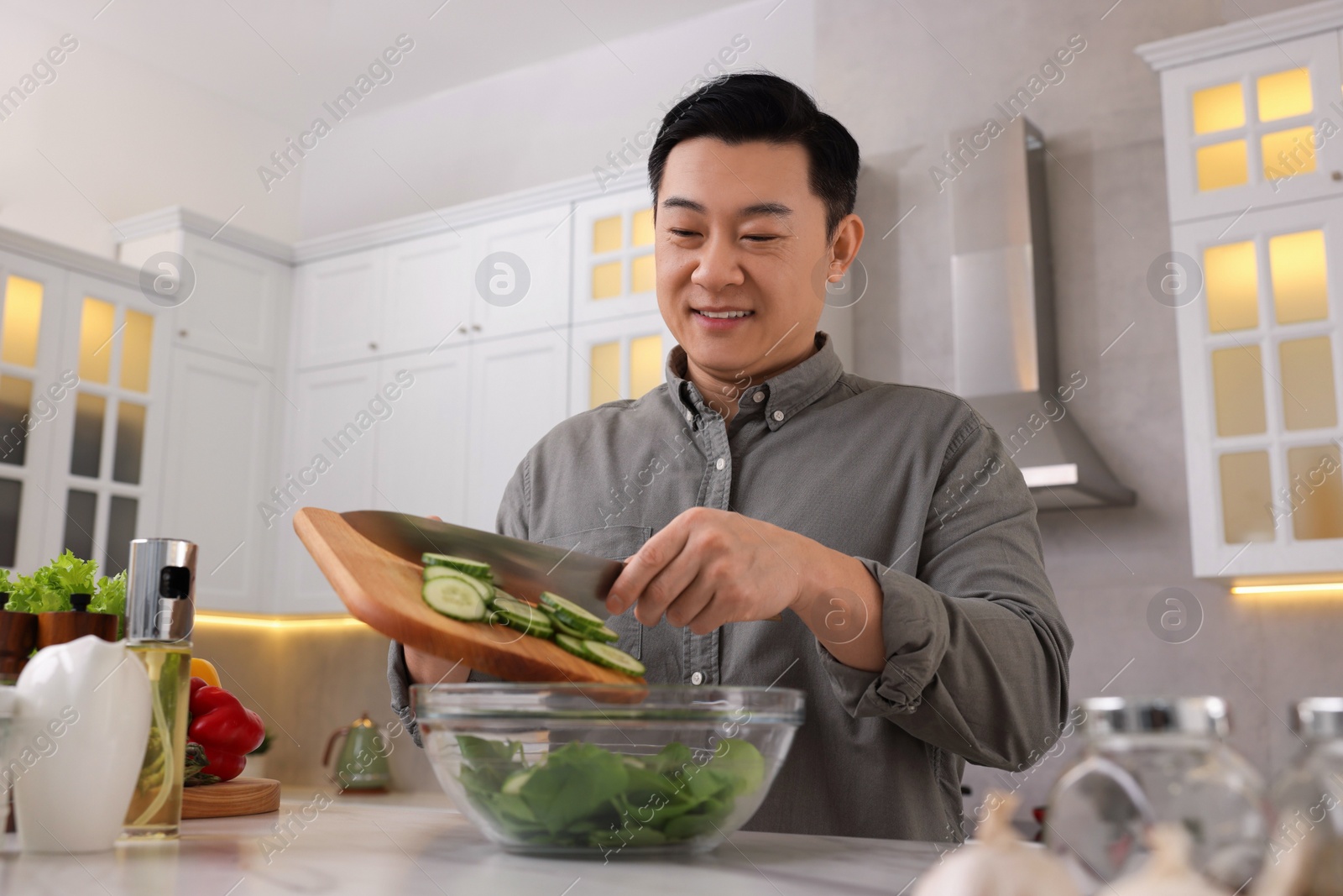 Photo of Cooking process. Man adding cut cucumber into bowl in kitchen, low angle view