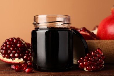 Glass jar of tasty pomegranate sauce and fresh ripe fruit on wooden table