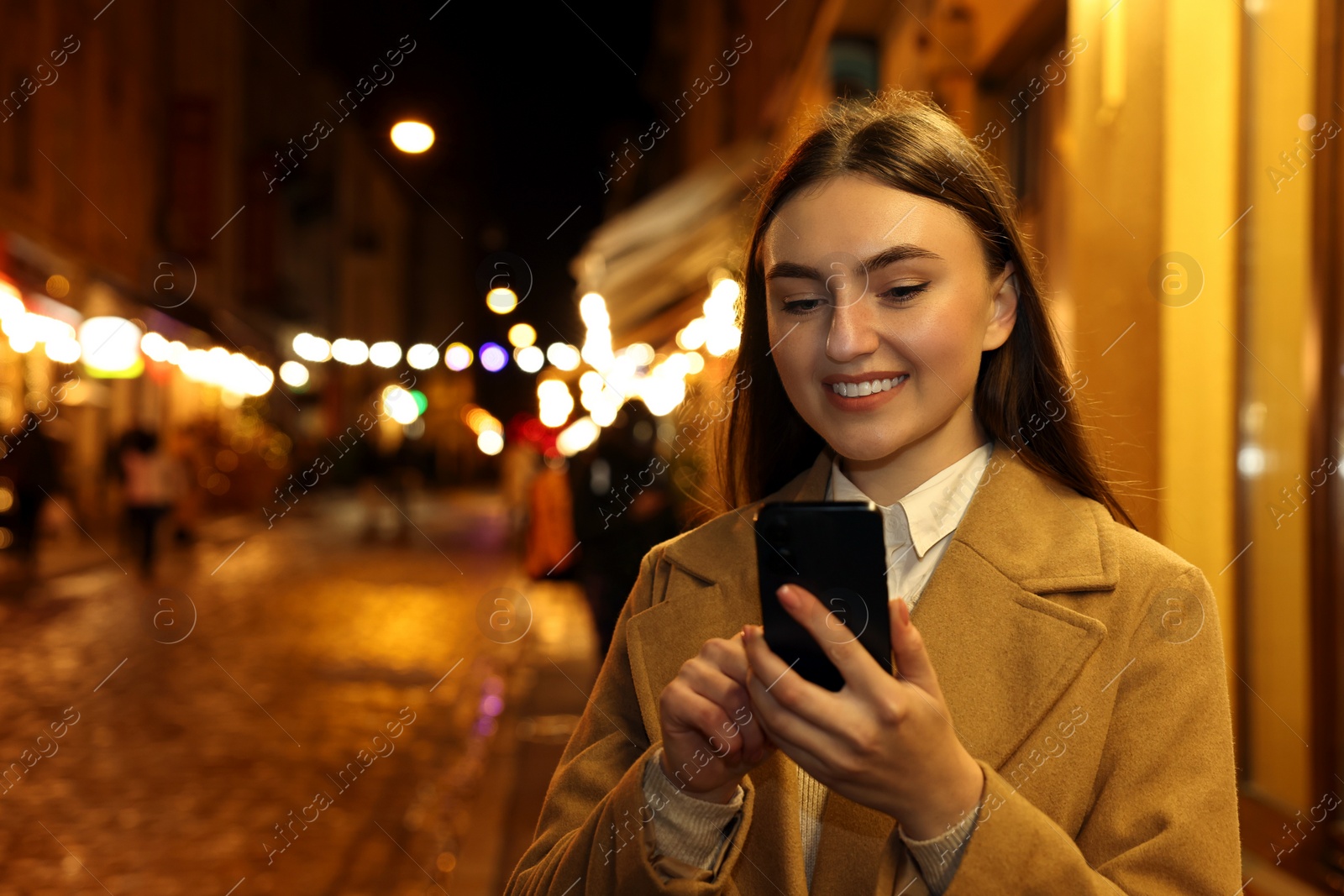 Photo of Smiling woman using smartphone on night city street. Space for text