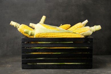 Photo of Wooden crate with tasty fresh corn cobs on grey table