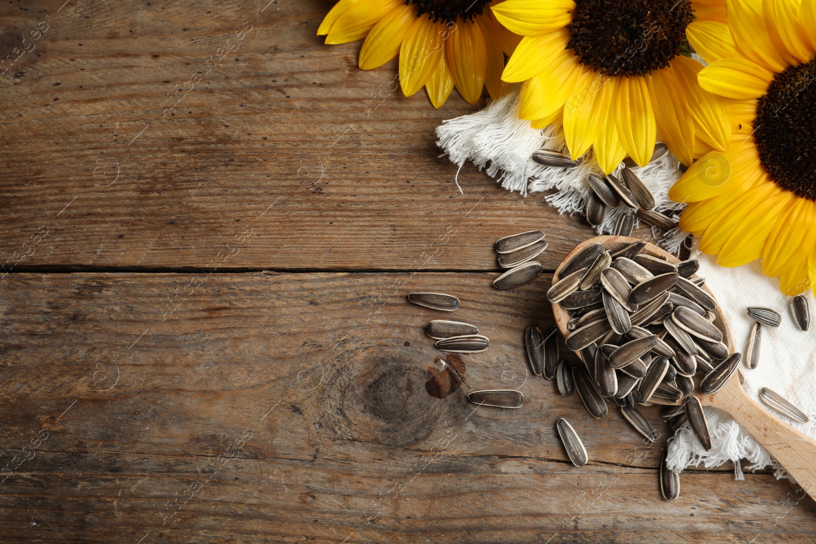 Photo of Organic sunflower seeds and flowers on wooden table, flat lay. Space for text