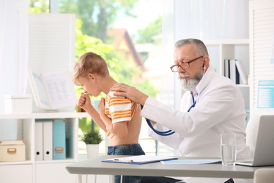 Photo of Doctor examining coughing little boy at clinic