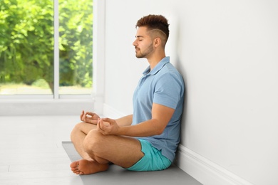 Photo of Young man practicing zen yoga near wall indoors