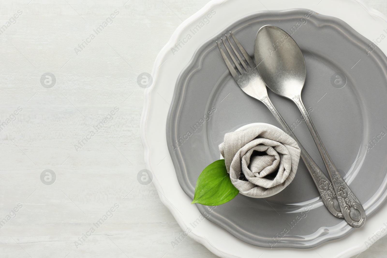 Photo of Stylish setting with cutlery, napkin, leaf and plates on light textured table, top view. Space for text