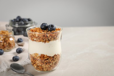 Photo of Glass of yogurt with granola and blueberries on grey marble table, closeup. Space for text