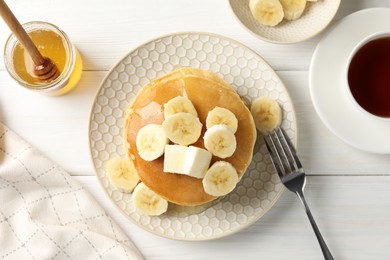 Photo of Delicious pancakes with bananas, honey and butter served with tea on white wooden table, flat lay