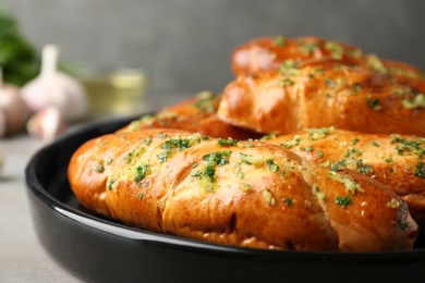 Photo of Plate of bread loaves with garlic and herbs on grey table, closeup