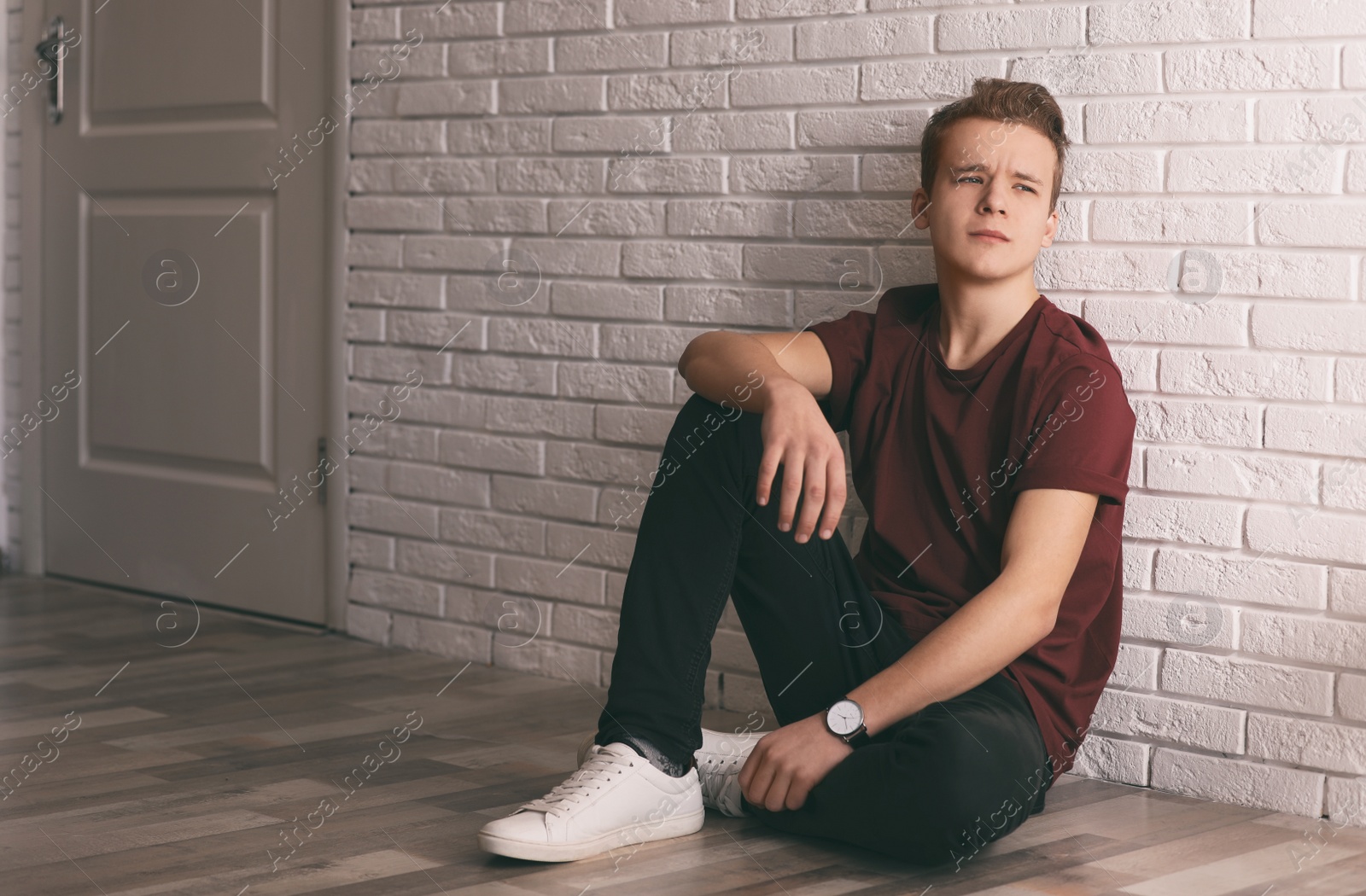 Photo of Upset teenage boy sitting alone on floor near wall