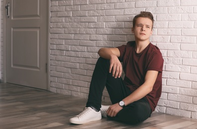 Upset teenage boy sitting alone on floor near wall