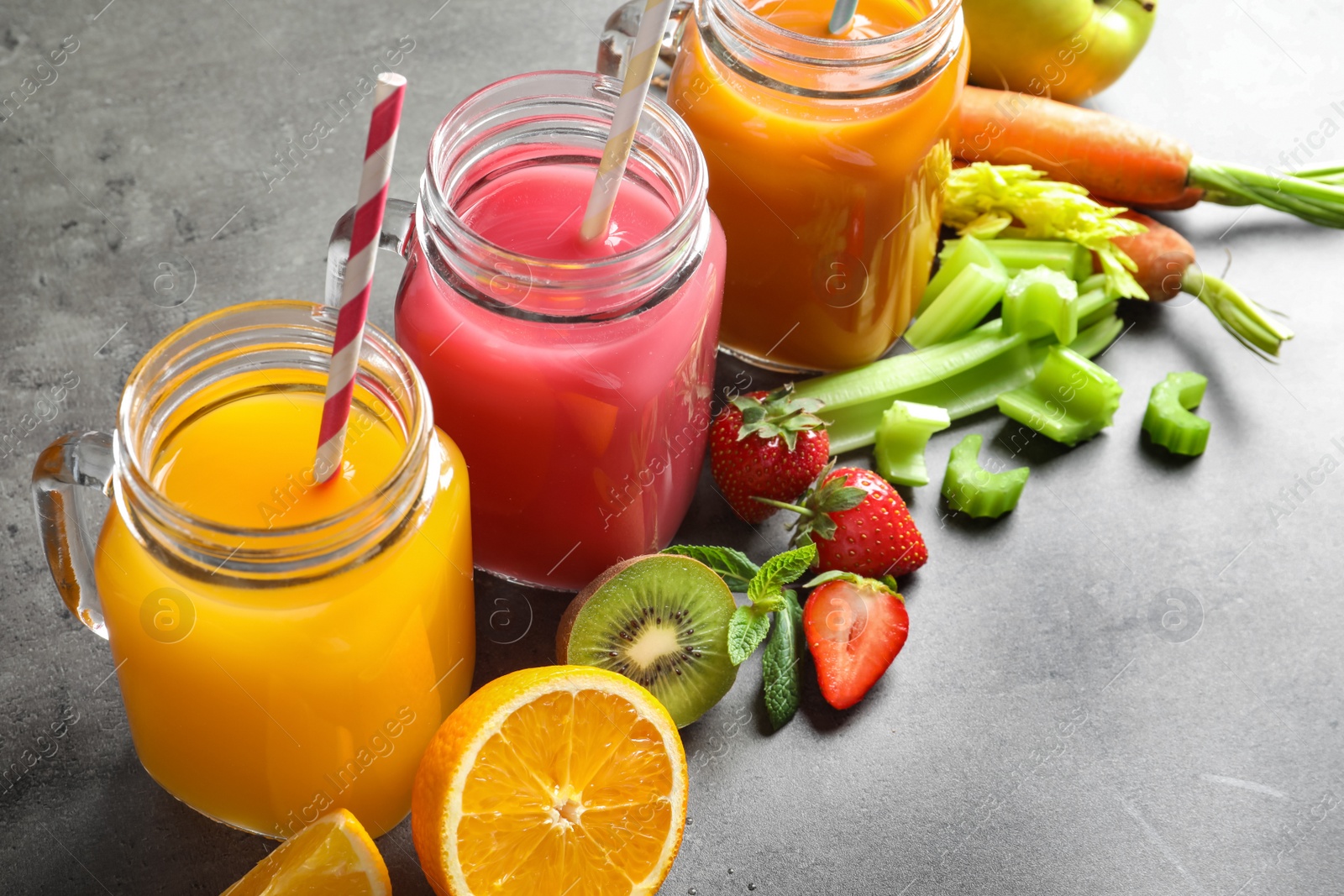 Photo of Mason jars with different juices and fresh ingredients on table