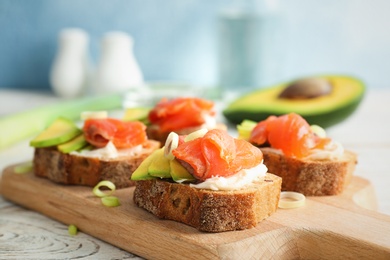 Photo of Tasty sandwiches with fresh sliced salmon fillet and avocado on wooden board, closeup