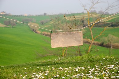 Photo of Blank wooden board hanging on rope in countryside. Space for text
